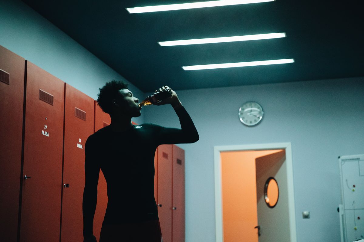 Silhouette eines Sportlers, der in einer Umkleide mit roten Spinden aus einer Flasche trinkt
