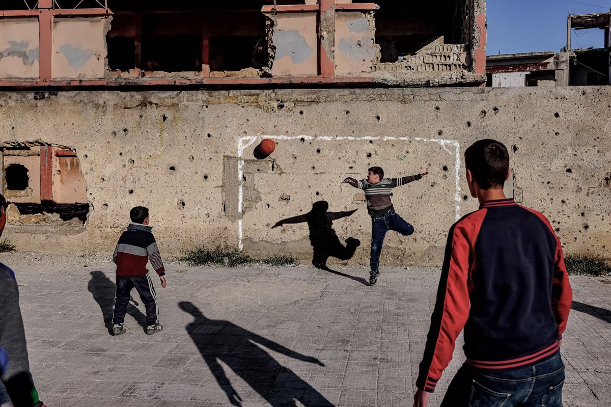 Buben spielen Fußball vor einer von Einschüssen gezeichneten Wand